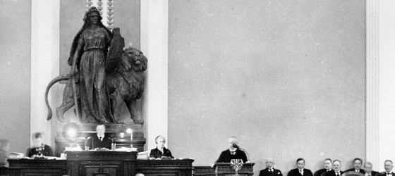 Ett svartvit foto av Heimolahusets sal där Väinö Tanner talar från talarstolen.