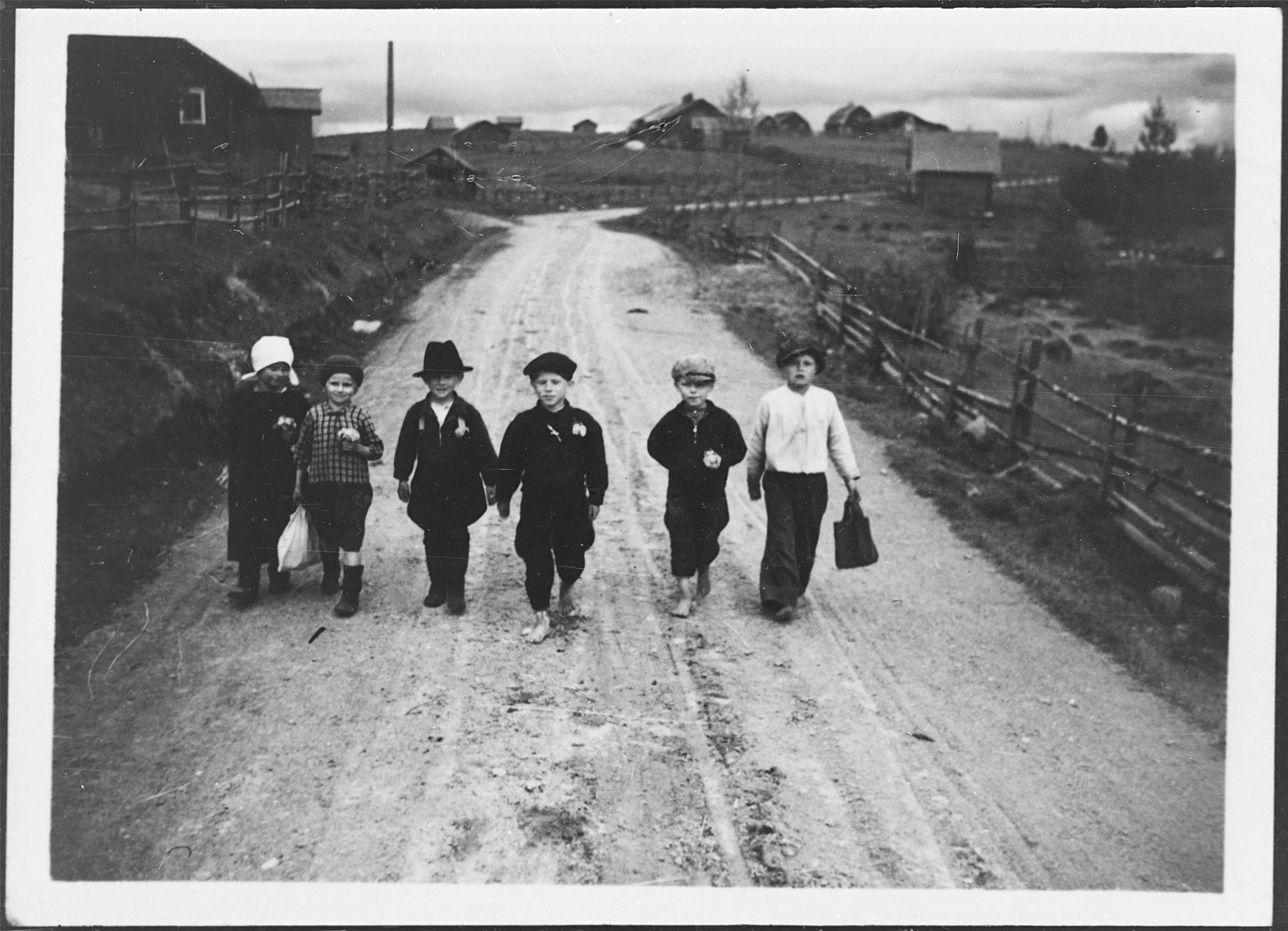 Valokuvassa kuusi pientä koululaista kävelee rinnakkain koulumatkalla.