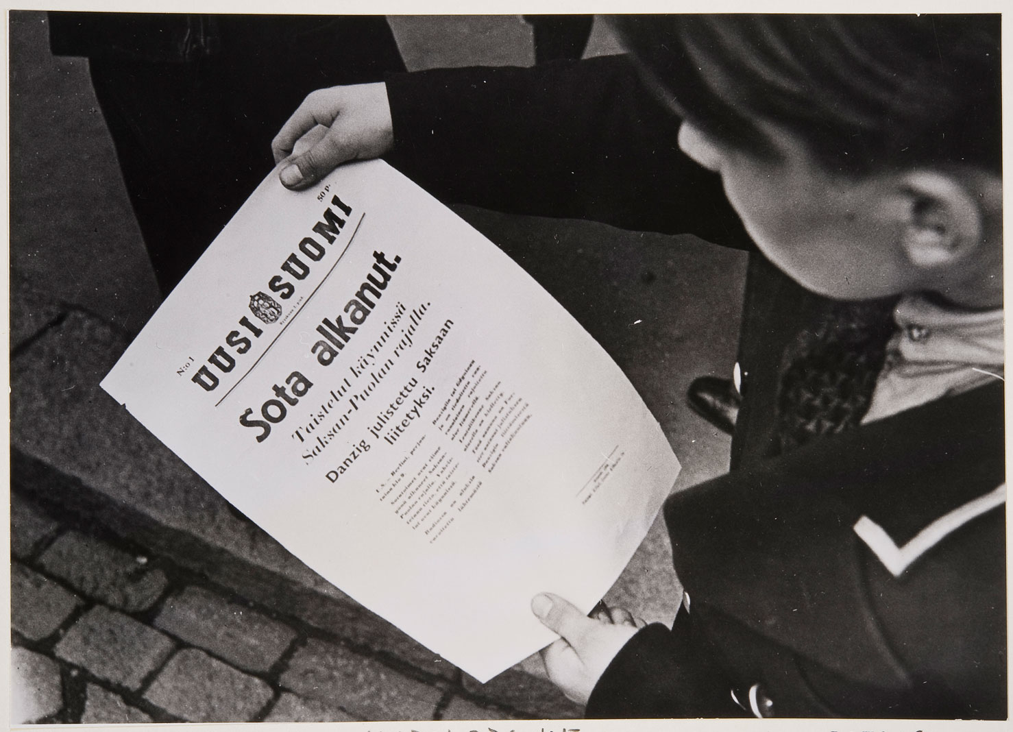 Valokuvassa Uuden Suomen tiedote sodan syttymisestä 1.9.1939 nuoren miehen kädessä.